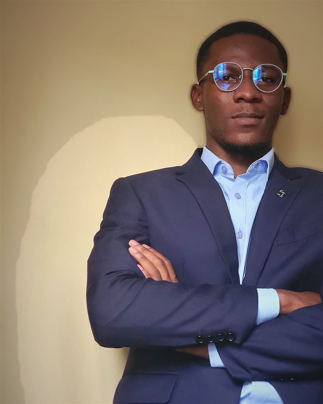 Portrait of Tolulope Ajidahun standing with arms crossed in a navy suit